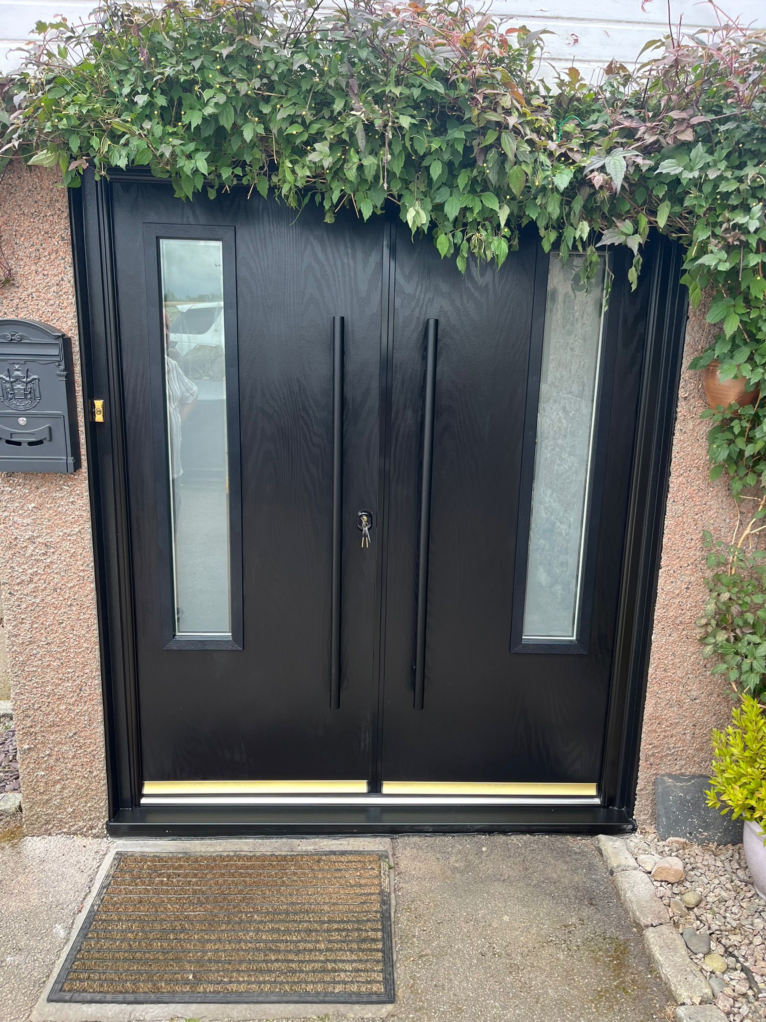 Black double composite doors framed by ivy